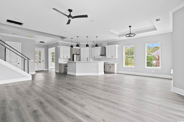 unfurnished living room with ceiling fan with notable chandelier, a raised ceiling, light wood-type flooring, and crown molding