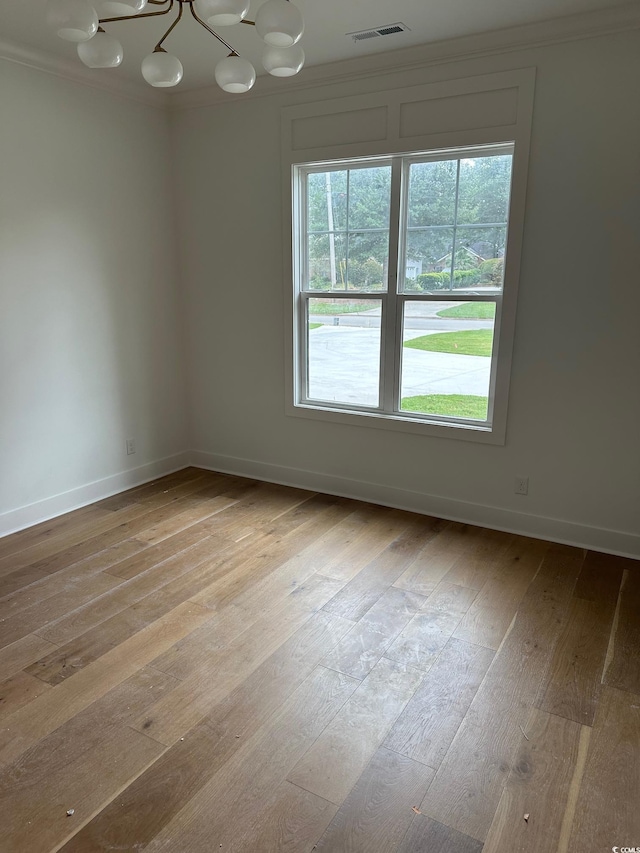 spare room featuring light wood-type flooring, an inviting chandelier, and crown molding