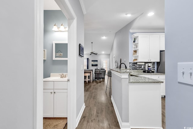 kitchen with kitchen peninsula, white cabinets, ceiling fan, and sink