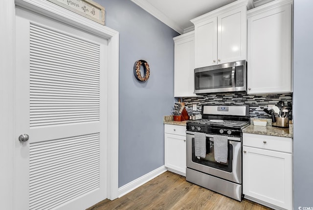 kitchen with crown molding, appliances with stainless steel finishes, white cabinetry, light stone counters, and wood-type flooring