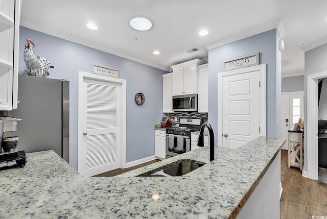 kitchen with light stone countertops, ornamental molding, stainless steel appliances, sink, and white cabinetry