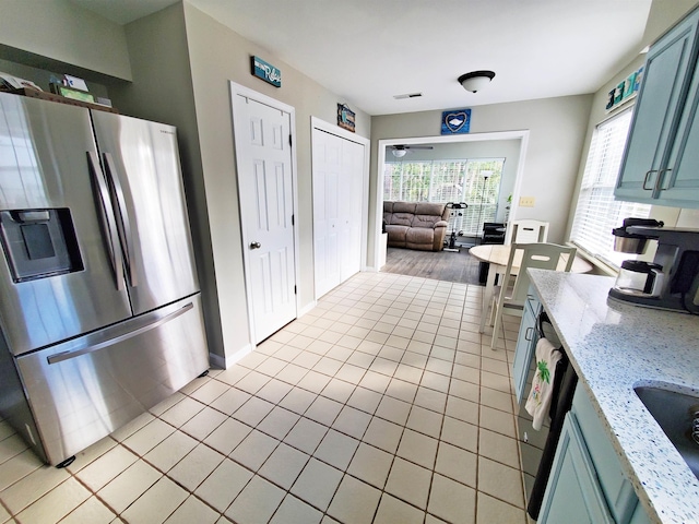 kitchen with light tile patterned floors, stainless steel fridge, blue cabinets, and light stone counters