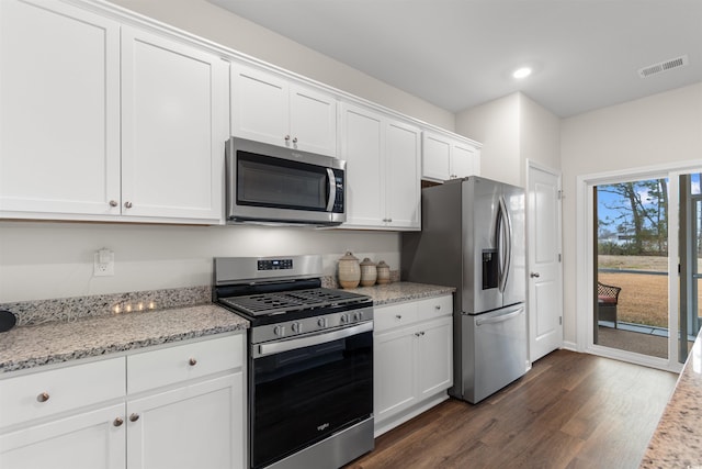 kitchen with light stone countertops, appliances with stainless steel finishes, white cabinetry, and dark wood-type flooring