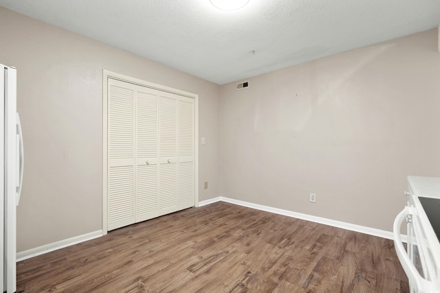 unfurnished bedroom with hardwood / wood-style flooring, a closet, a textured ceiling, and white fridge