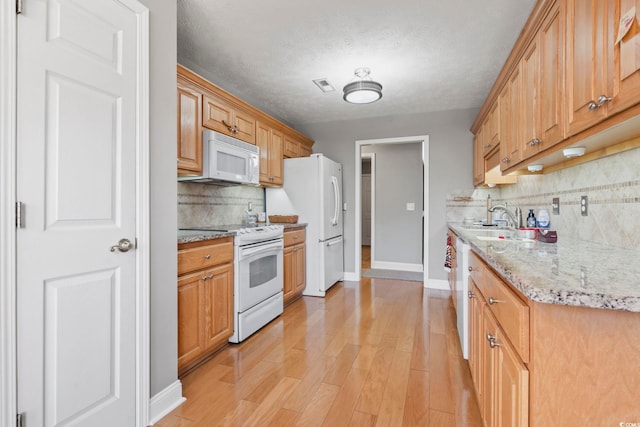 kitchen with tasteful backsplash, sink, white appliances, light stone countertops, and light wood-type flooring