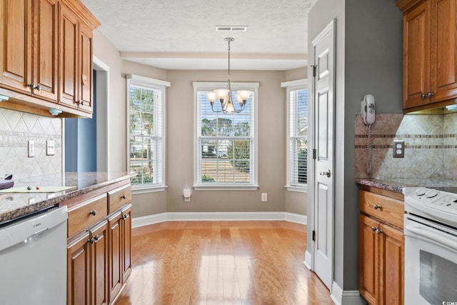 kitchen featuring white appliances, dark stone counters, decorative light fixtures, and light hardwood / wood-style floors