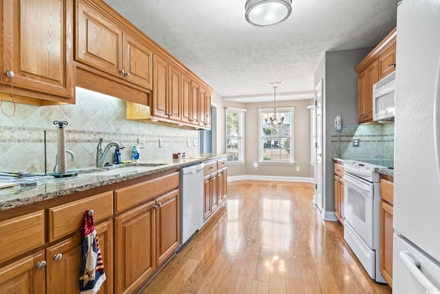 kitchen with pendant lighting, sink, white appliances, light hardwood / wood-style flooring, and light stone counters