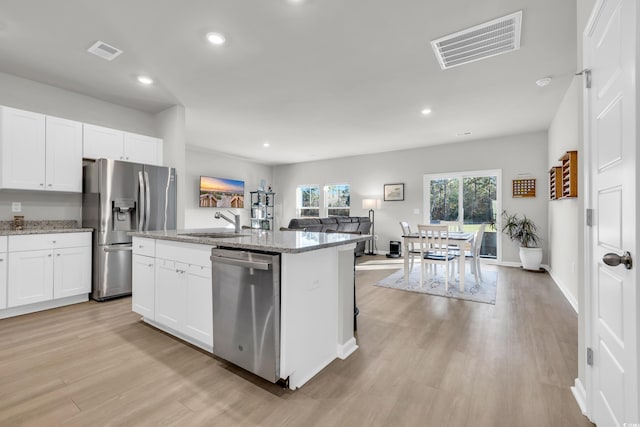 kitchen with light stone countertops, a center island with sink, white cabinets, appliances with stainless steel finishes, and sink