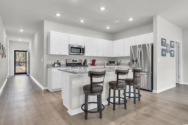 kitchen with white cabinetry, light stone counters, a kitchen bar, a center island with sink, and appliances with stainless steel finishes