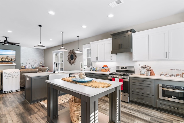 kitchen with stainless steel gas stove, dark hardwood / wood-style floors, white cabinets, a kitchen island, and decorative light fixtures