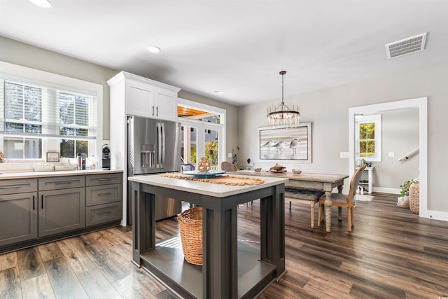 kitchen with dark wood-type flooring, stainless steel fridge, white cabinetry, hanging light fixtures, and a notable chandelier