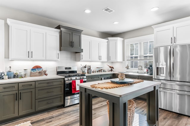 kitchen featuring backsplash, wood-type flooring, white cabinets, and appliances with stainless steel finishes