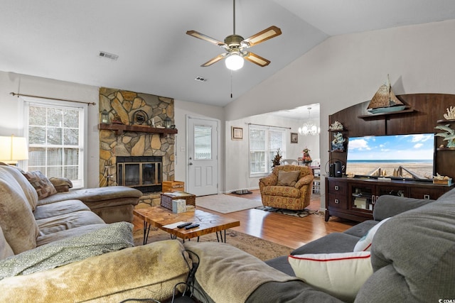 living room with vaulted ceiling, a stone fireplace, ceiling fan with notable chandelier, and light wood-type flooring