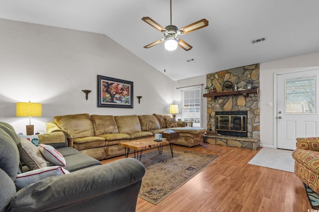 living room with a stone fireplace, vaulted ceiling, a healthy amount of sunlight, and hardwood / wood-style flooring