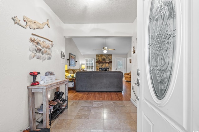 foyer with ceiling fan, a fireplace, vaulted ceiling, and a textured ceiling