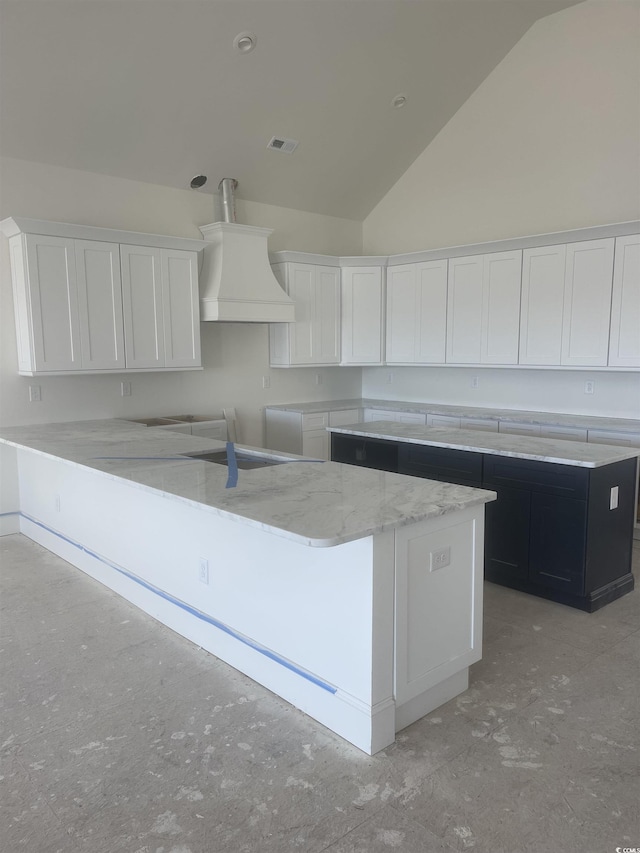 kitchen with custom exhaust hood, visible vents, white cabinets, a kitchen island, and dark cabinets