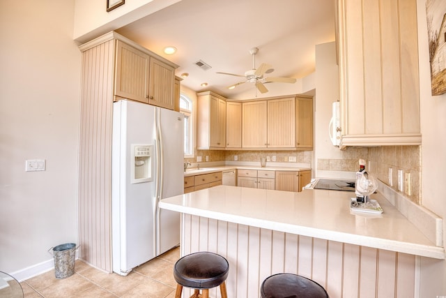 kitchen with kitchen peninsula, white appliances, a kitchen bar, decorative backsplash, and light brown cabinetry