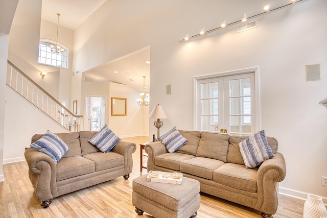 living room with crown molding, a towering ceiling, a chandelier, and light wood-type flooring