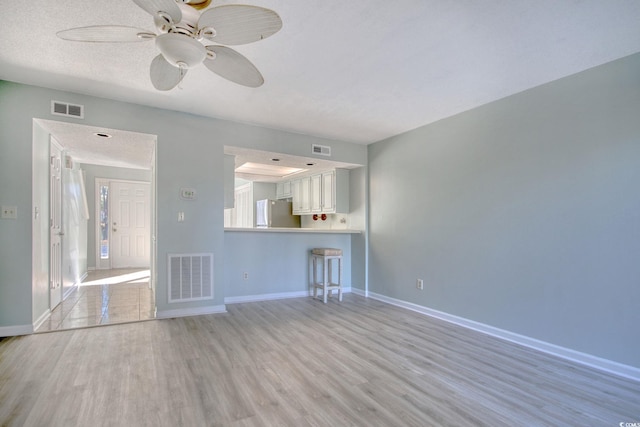 unfurnished living room featuring a textured ceiling, ceiling fan, and light hardwood / wood-style floors