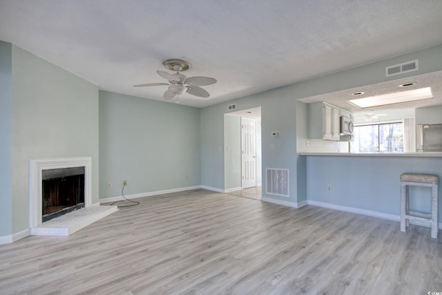 unfurnished living room featuring a textured ceiling, ceiling fan, and light hardwood / wood-style floors