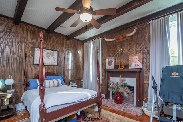 bedroom featuring ceiling fan, wood-type flooring, beamed ceiling, and wood walls