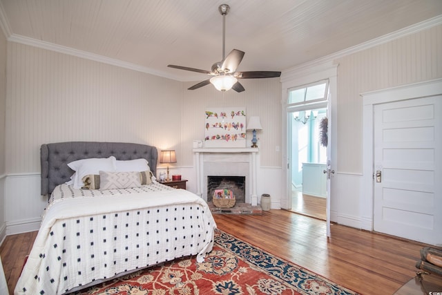 bedroom with ceiling fan, hardwood / wood-style flooring, crown molding, and a fireplace