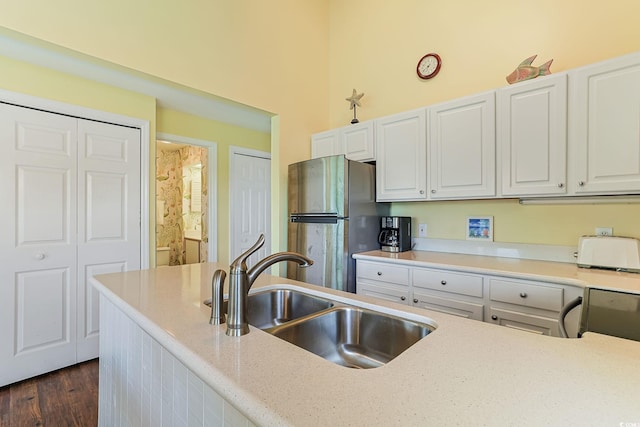 kitchen featuring stainless steel fridge, light stone counters, white cabinetry, and sink