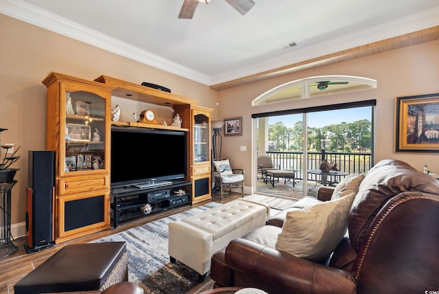 living area with a ceiling fan, wood finished floors, baseboards, visible vents, and crown molding