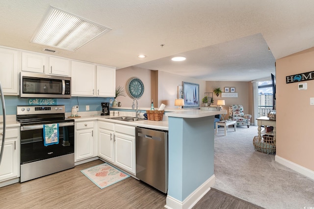 kitchen with kitchen peninsula, stainless steel appliances, light colored carpet, sink, and white cabinets