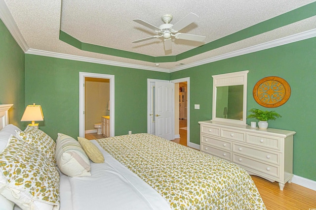 bedroom featuring a raised ceiling, ensuite bath, ceiling fan, and ornamental molding