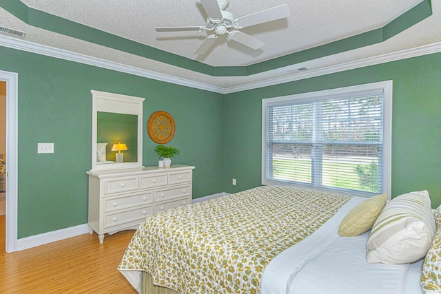 bedroom featuring a raised ceiling, light hardwood / wood-style flooring, ceiling fan, ornamental molding, and a textured ceiling