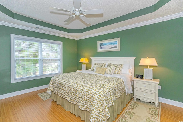 bedroom featuring ceiling fan, crown molding, a textured ceiling, a tray ceiling, and light wood-type flooring