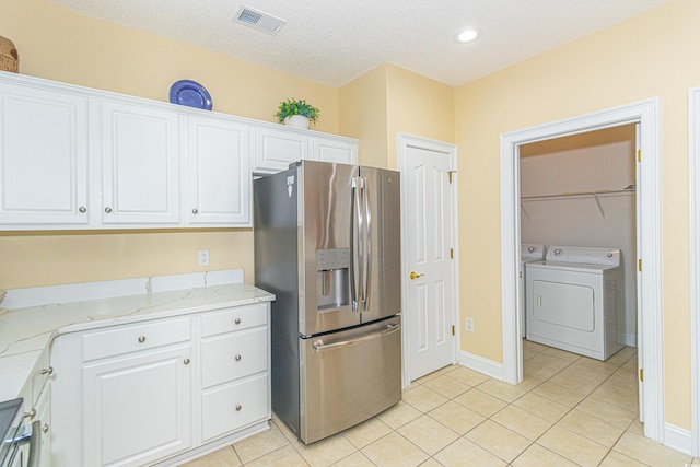 kitchen featuring washing machine and dryer, light stone counters, white cabinets, stainless steel refrigerator with ice dispenser, and light tile patterned floors