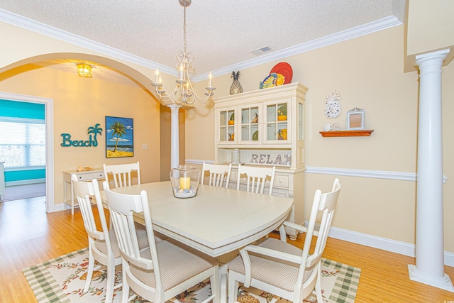 dining room featuring ornate columns, light hardwood / wood-style floors, a textured ceiling, and an inviting chandelier