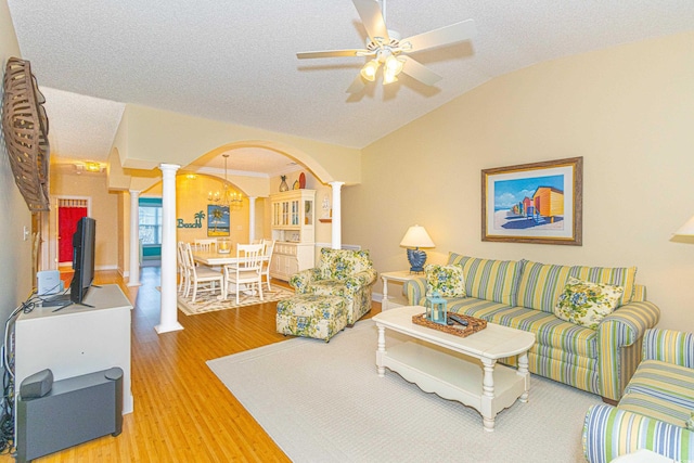 living room featuring hardwood / wood-style floors, lofted ceiling, ceiling fan with notable chandelier, a textured ceiling, and decorative columns