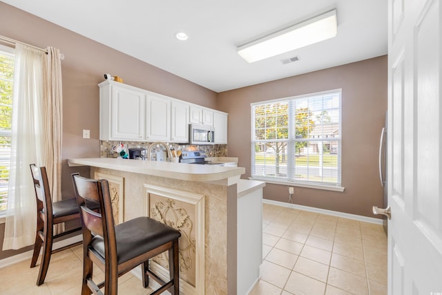 kitchen featuring white cabinetry, kitchen peninsula, a kitchen bar, decorative backsplash, and appliances with stainless steel finishes