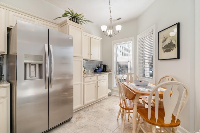 kitchen with decorative light fixtures, tasteful backsplash, stainless steel fridge, a chandelier, and light stone counters