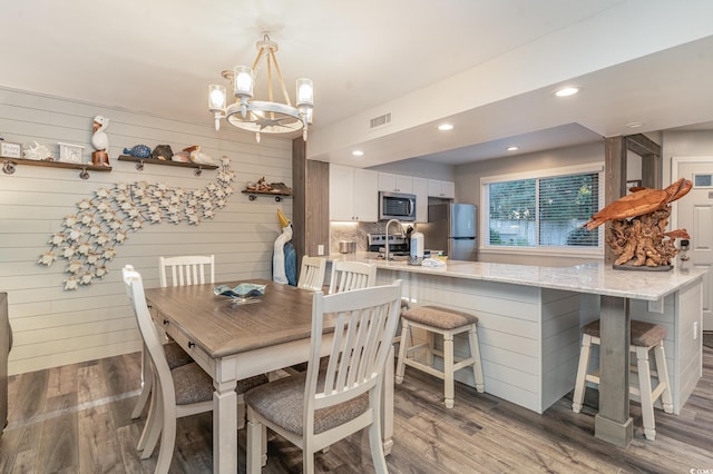 dining room with wood walls, light hardwood / wood-style floors, sink, and an inviting chandelier