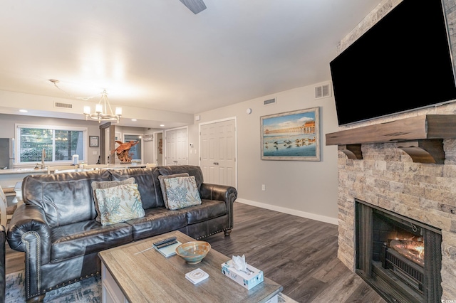 living room featuring a stone fireplace, dark wood-type flooring, and a chandelier