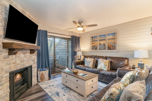 living room featuring wood-type flooring, a stone fireplace, ceiling fan, and wood walls