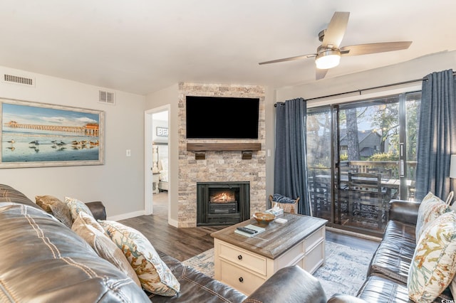 living room featuring a stone fireplace, ceiling fan, and dark wood-type flooring