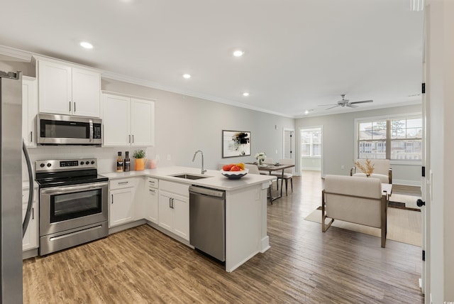 kitchen with sink, stainless steel appliances, kitchen peninsula, wood-type flooring, and white cabinets