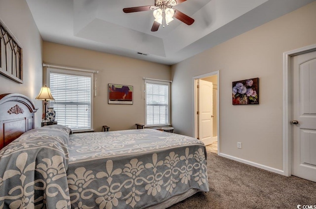 bedroom with ceiling fan, a raised ceiling, carpet floors, and ensuite bath