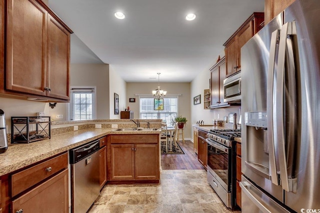 kitchen featuring kitchen peninsula, appliances with stainless steel finishes, sink, pendant lighting, and an inviting chandelier