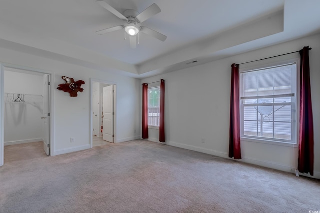 unfurnished bedroom with a closet, ceiling fan, a tray ceiling, and a spacious closet