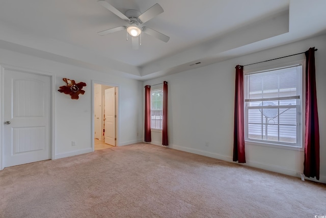 carpeted empty room with a raised ceiling and ceiling fan