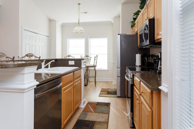 kitchen featuring dark stone countertops, light hardwood / wood-style floors, stainless steel appliances, hanging light fixtures, and sink