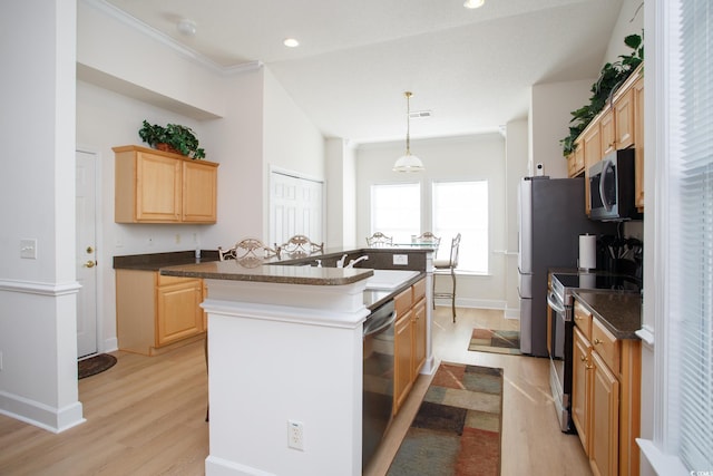 kitchen featuring a center island with sink, appliances with stainless steel finishes, hanging light fixtures, light hardwood / wood-style floors, and light brown cabinetry