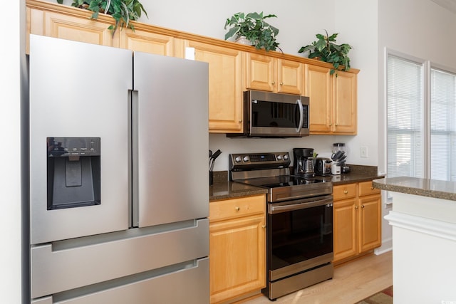 kitchen with stainless steel appliances, light wood-type flooring, light brown cabinets, and dark stone counters