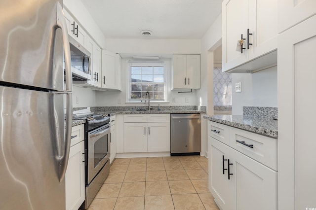 kitchen featuring light stone countertops, white cabinets, appliances with stainless steel finishes, sink, and light tile patterned floors